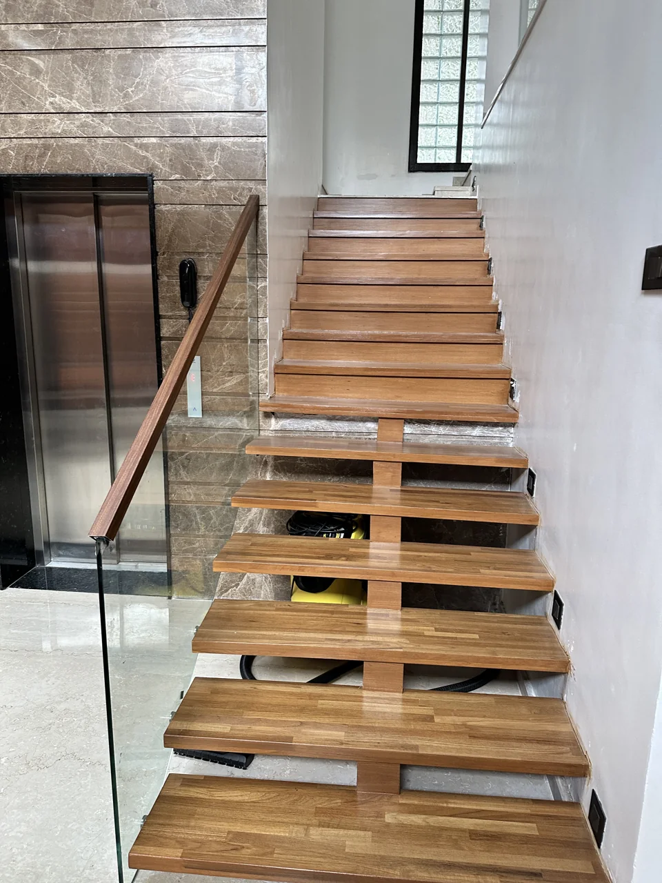 Timber cantilevered staircase with a glass balustrade beside a stone-clad wall