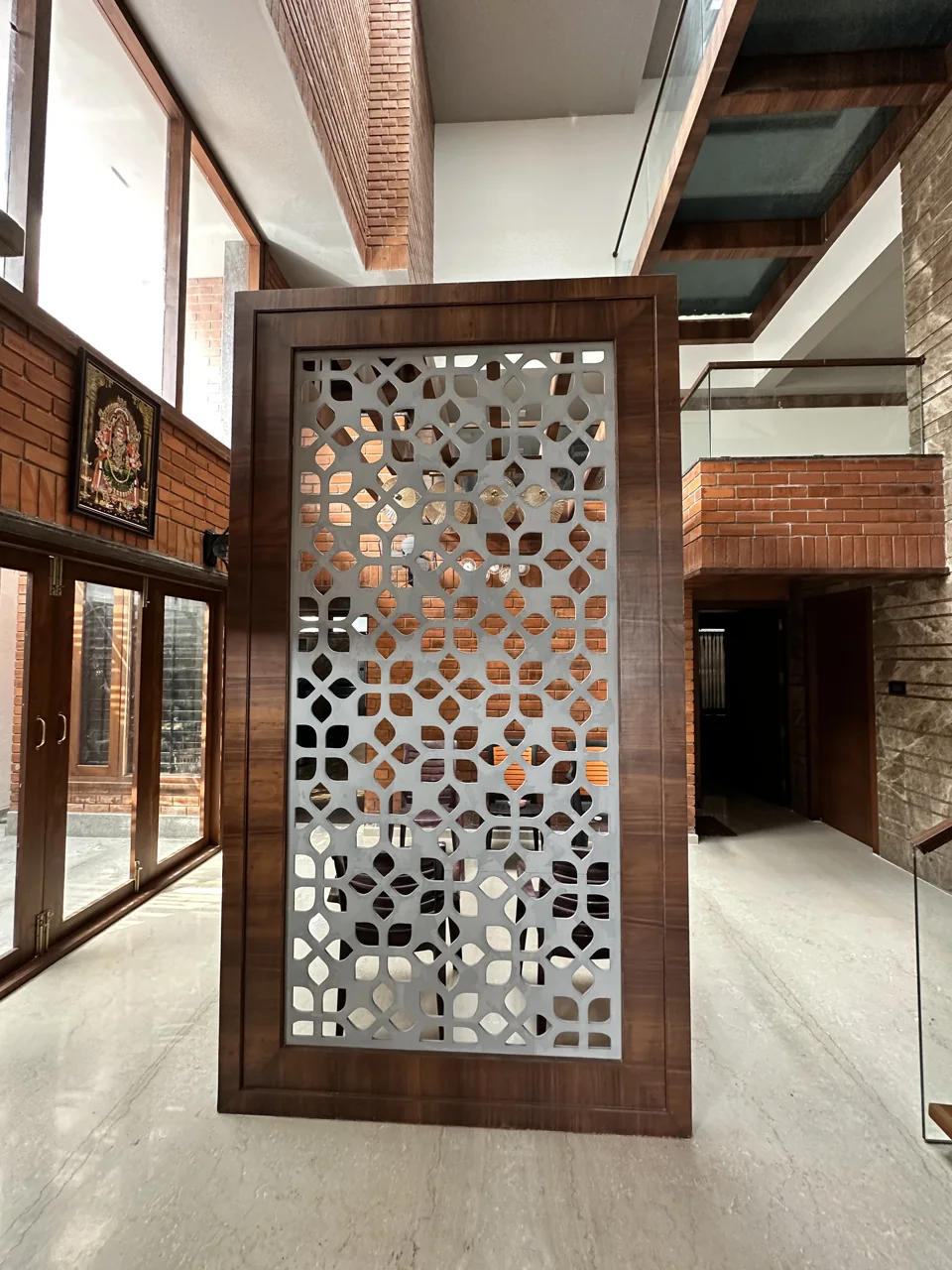 Timber-framed jaali partition standing in a brick and glass double-height hall