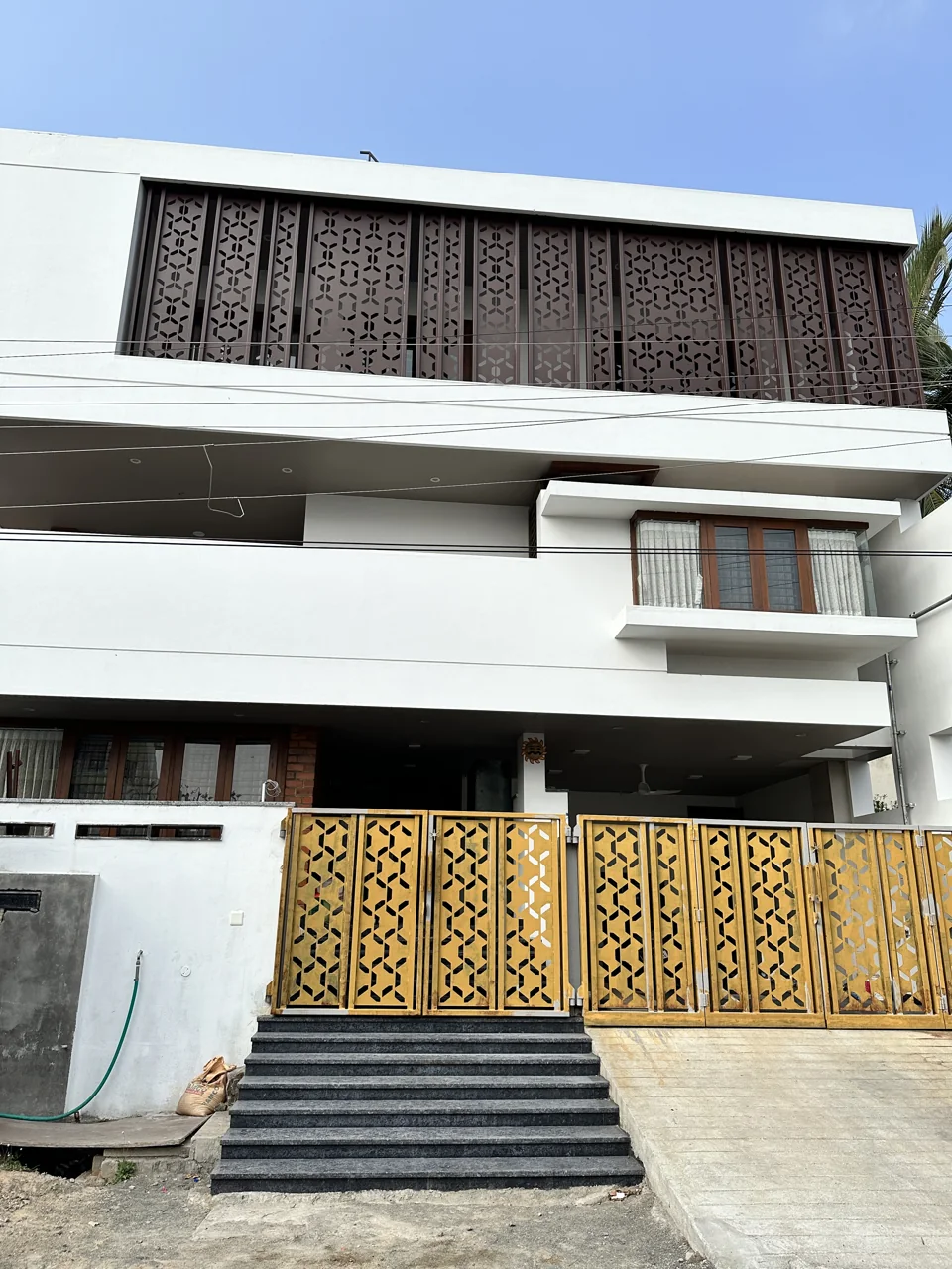 White two-storey home with a patterned metal screen across the upper floor and gold-finished gates